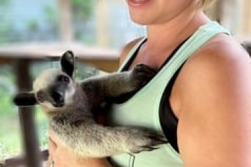 Woman smiling while holding a small lemur indoors.