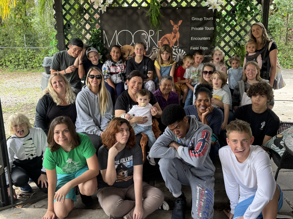 Group photo of diverse people, including adults and children, smiling under a pergola.