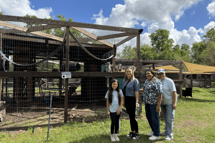 Four people stand smiling in front of a fenced animal enclosure.